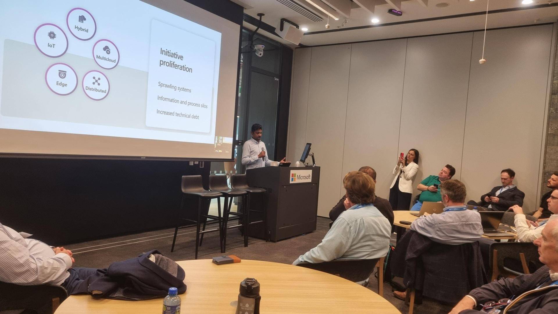 Palanikumar presents beside a large projected slide about hybrid, edge and multicloud environments, with attendees seated in the foreground.