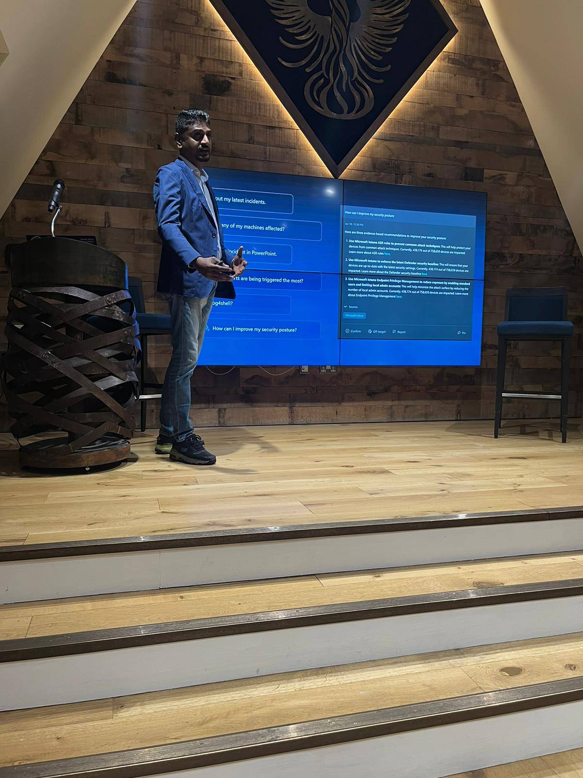 Palanikumar presents on a stage in front of large screens showing security questions and recommendations.